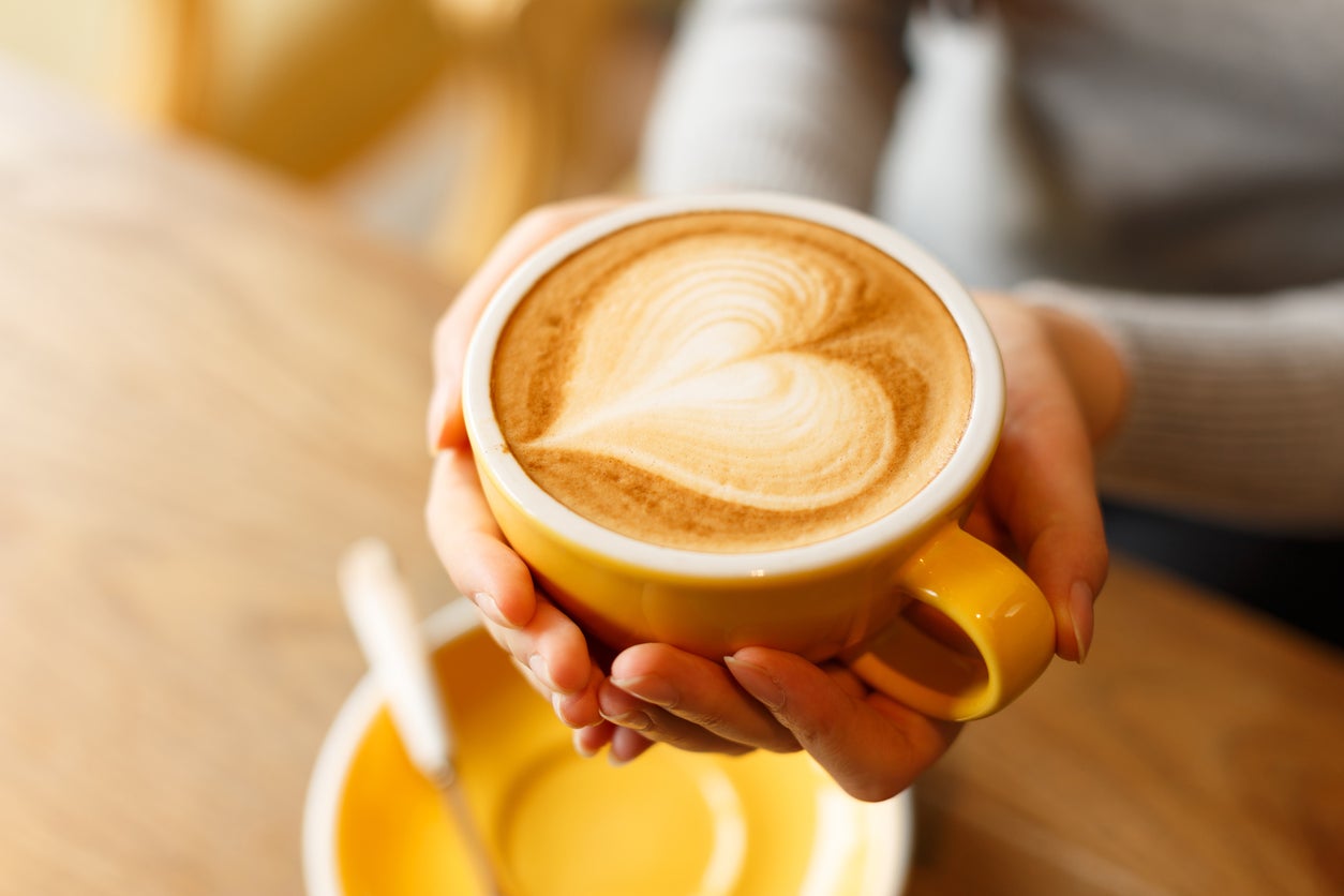 Holding a yellow cup of coffee with heart-shaped foam on top