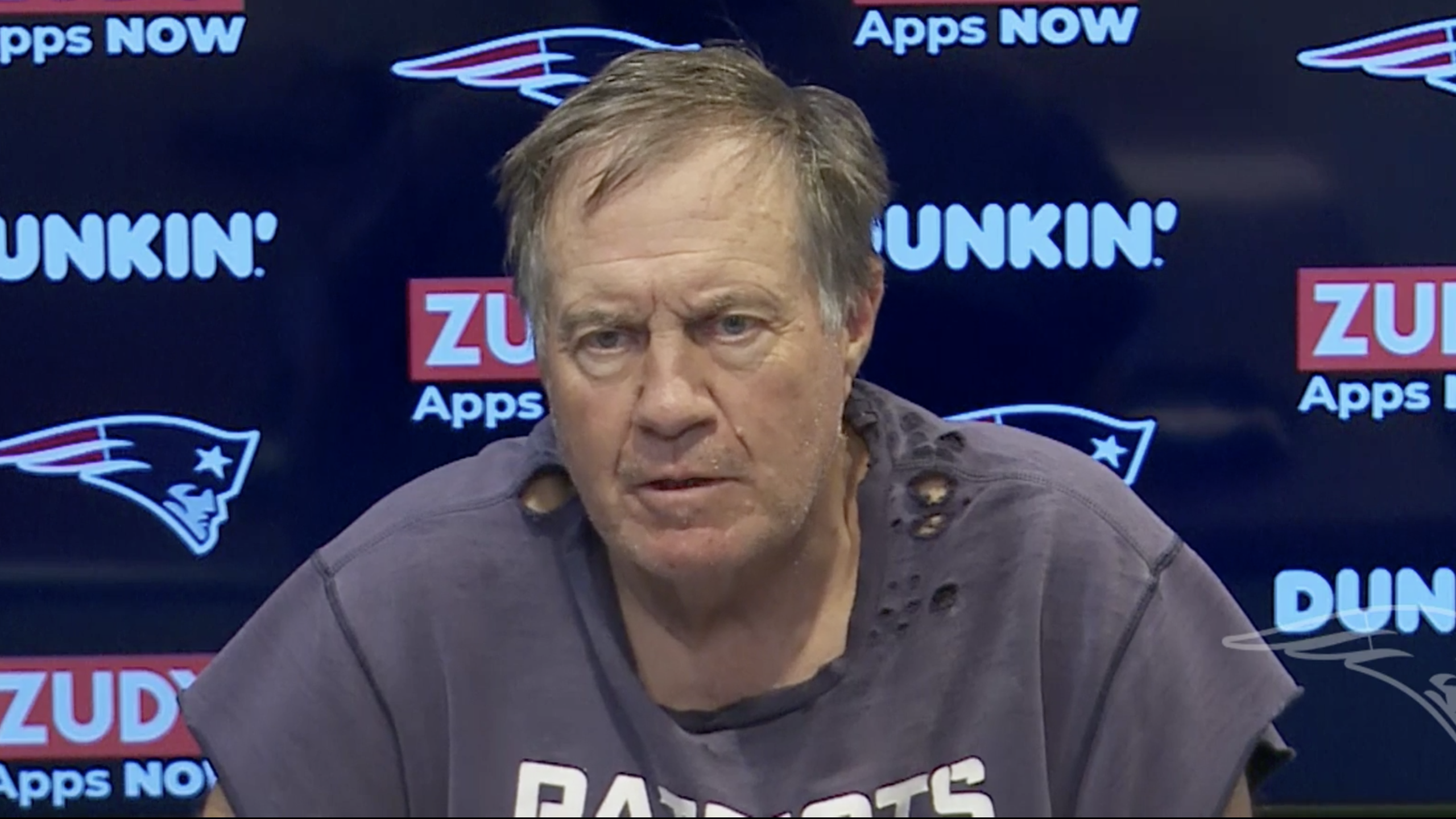 Bill Belichick during a conference wearing a t-shirt torn at the top